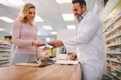 Customer handing a medical prescription to the pharmacist standing behind counter